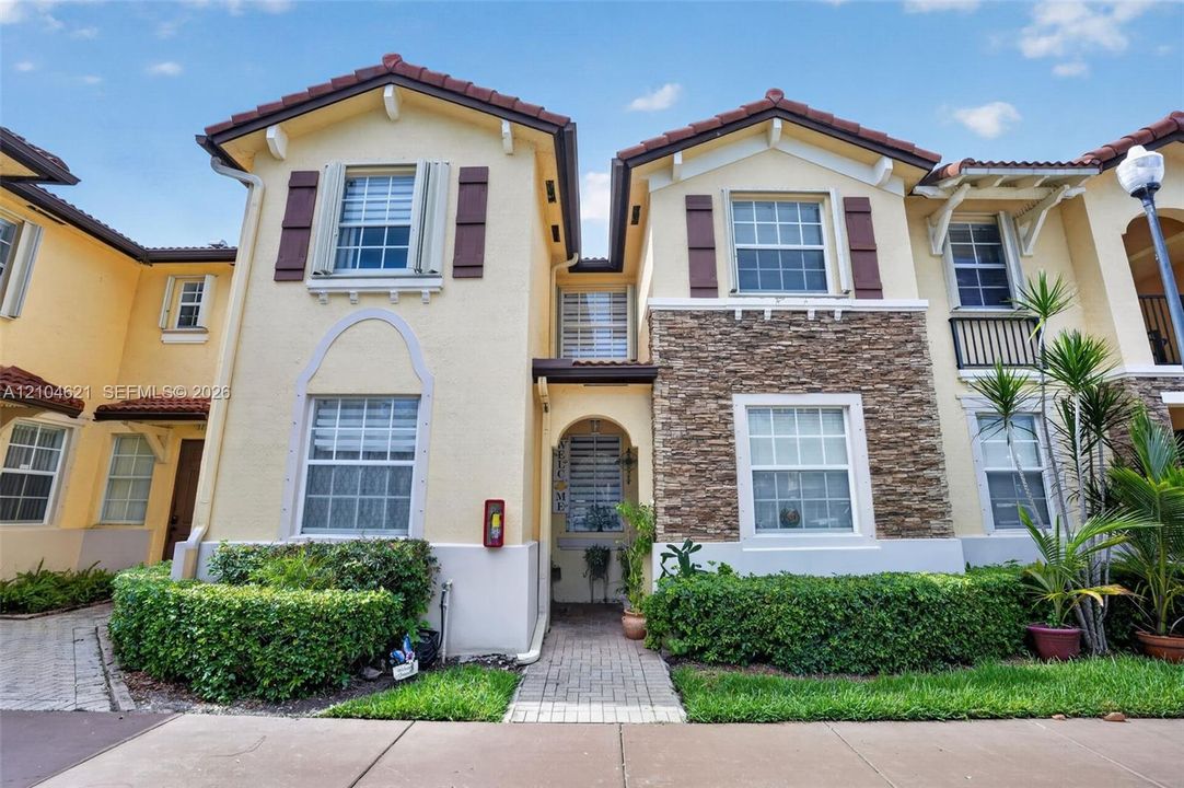 Multi-level exterior featuring stucco siding, stone veneer accents, decorative window shutters, and a tiled roof