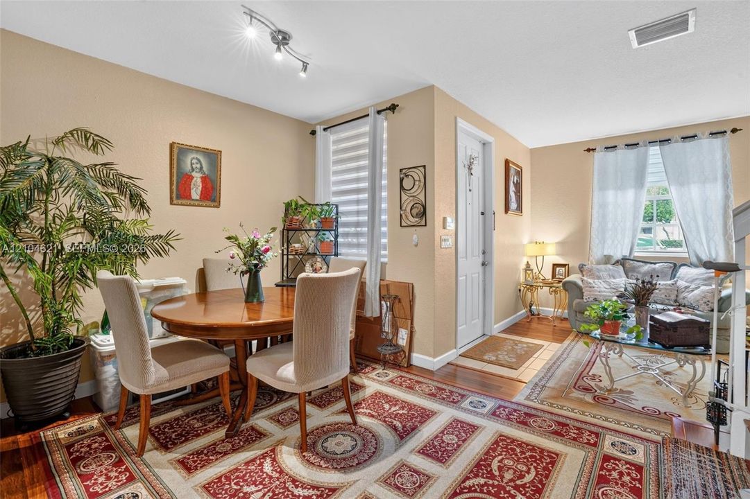 Open-concept interior featuring wood-finish flooring, multi-directional track lighting, and windows outfitted with dual-layered light-filtering shades