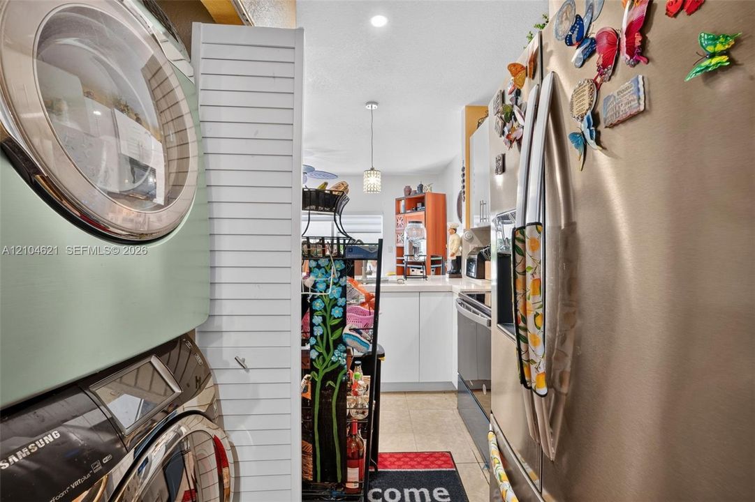 Stacked laundry appliances, stainless steel refrigerator, white louvered door, and recessed ceiling lighting