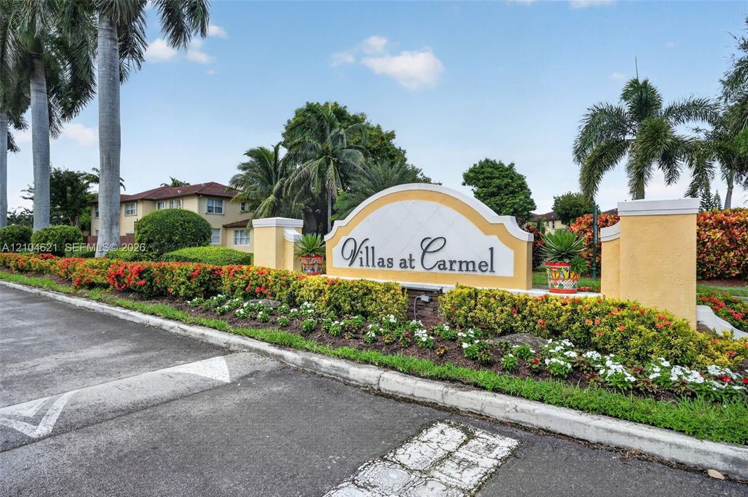 Entrance signage featuring stucco monuments, landscaped flower beds, mature palm trees, and paved asphalt road access