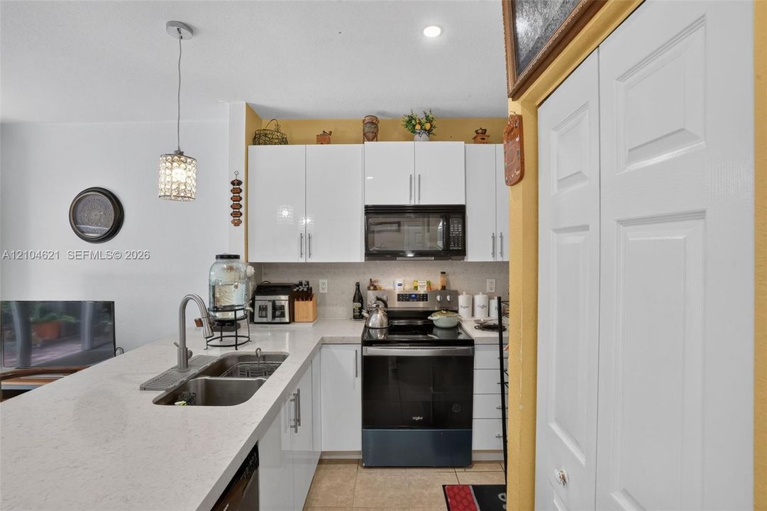 Kitchen featuring white gloss cabinetry, quartz countertops, a dual-basin stainless steel sink with high-arc faucet, a black electric range, and a pendant light fixture