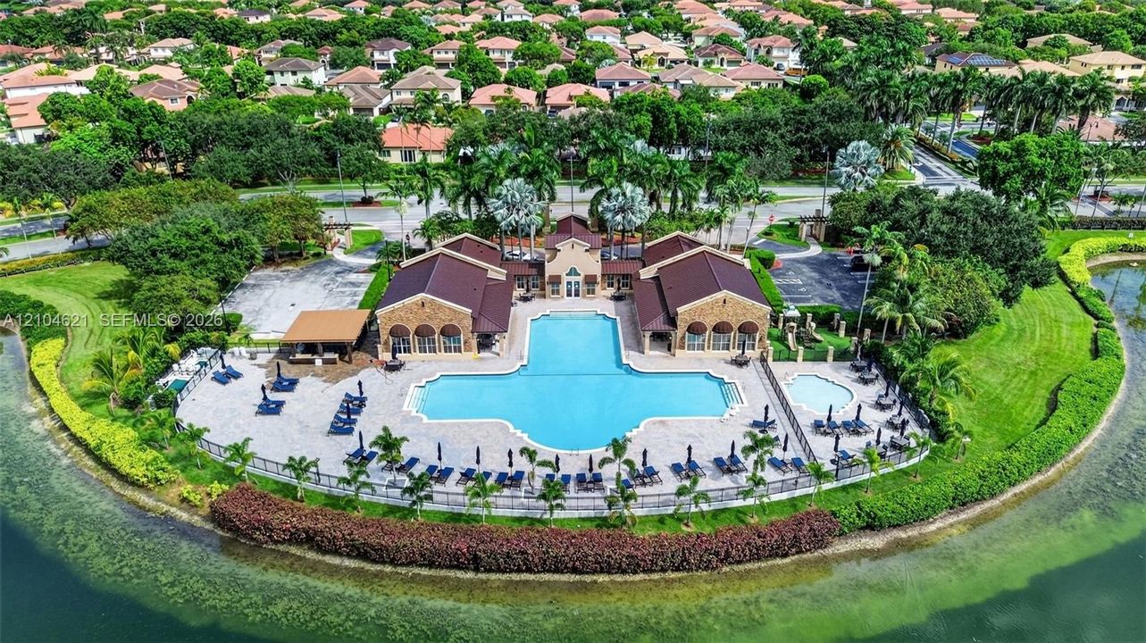 Community clubhouse featuring an expansive swimming pool, a separate spa, a shaded pavilion, and stone-paver decking, all situated along the waterfront