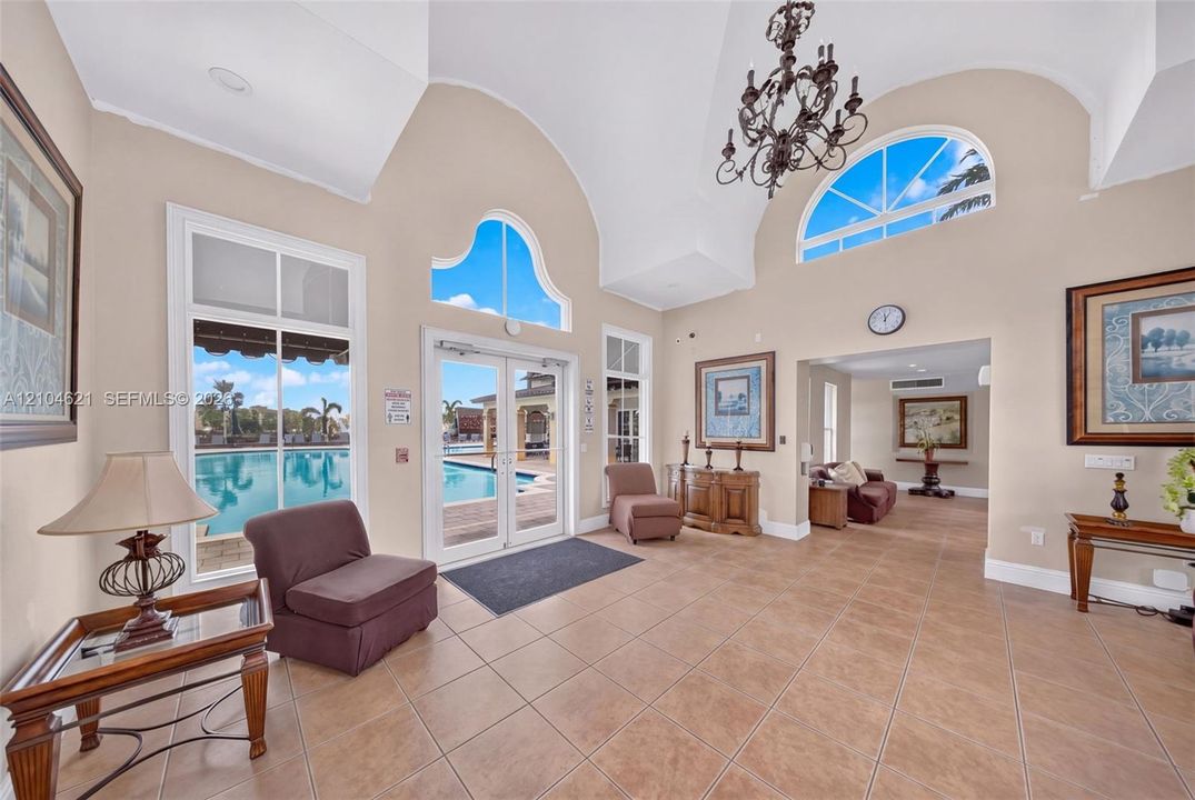 Vaulted ceilings featuring decorative arched windows and an ornate chandelier, complemented by tile flooring and double glass doors