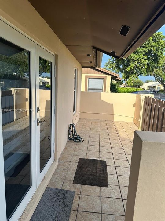 Covered patio featuring tiled flooring, white-framed glass doors, and a partial privacy wall