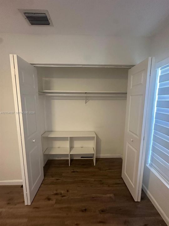 Integrated closet shelving with dual hanging rods, wood-finish flooring, and white bifold doors
