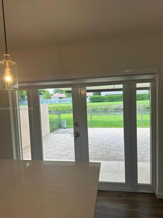 Glass pendant light fixture, wood-finish flooring, light-toned countertop, and double glass doors leading to a paver patio