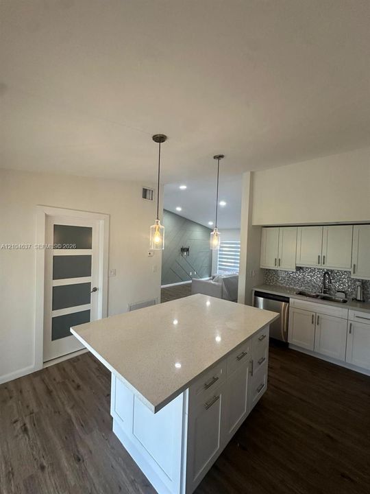 Central kitchen island with a light-colored countertop, wood-finish flooring, white cabinetry, and pendant lighting