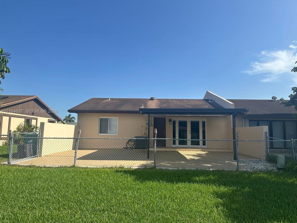 Rear exterior featuring a covered patio, chain-link fencing, and a grassy area