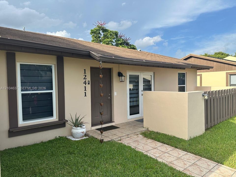 Stucco exterior with brown trim, covered front entry, tiled walkway, double-pane windows, and wood fencing