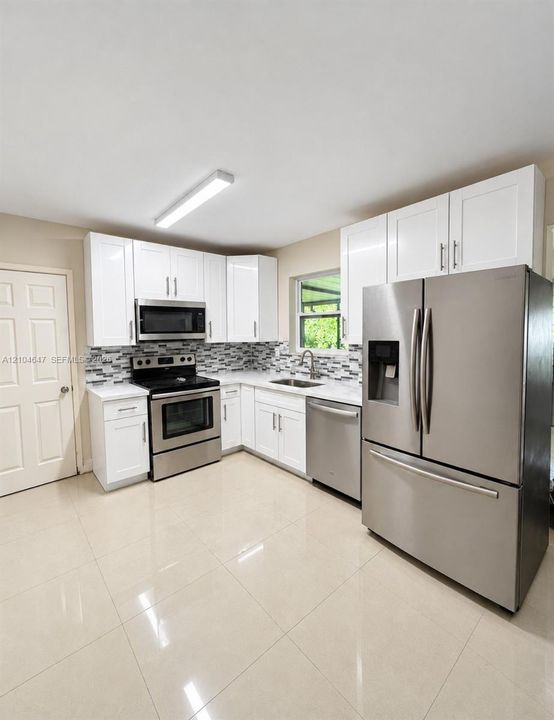 Kitchen featuring white shaker-style cabinetry, stainless steel appliances, multi-tonal mosaic tile backsplash, solid-surface countertops, and large-format tile flooring