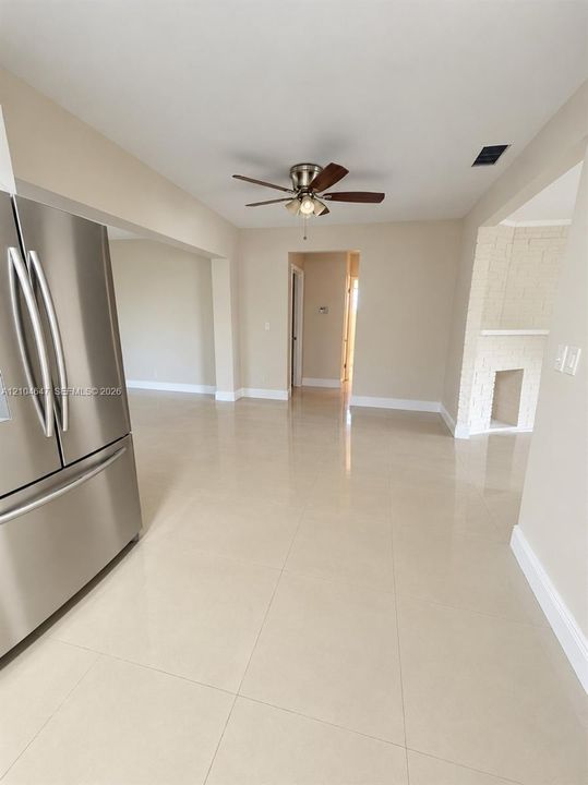 Large-format tile flooring, stainless steel refrigerator, ceiling fan with integrated lighting, and painted brick fireplace