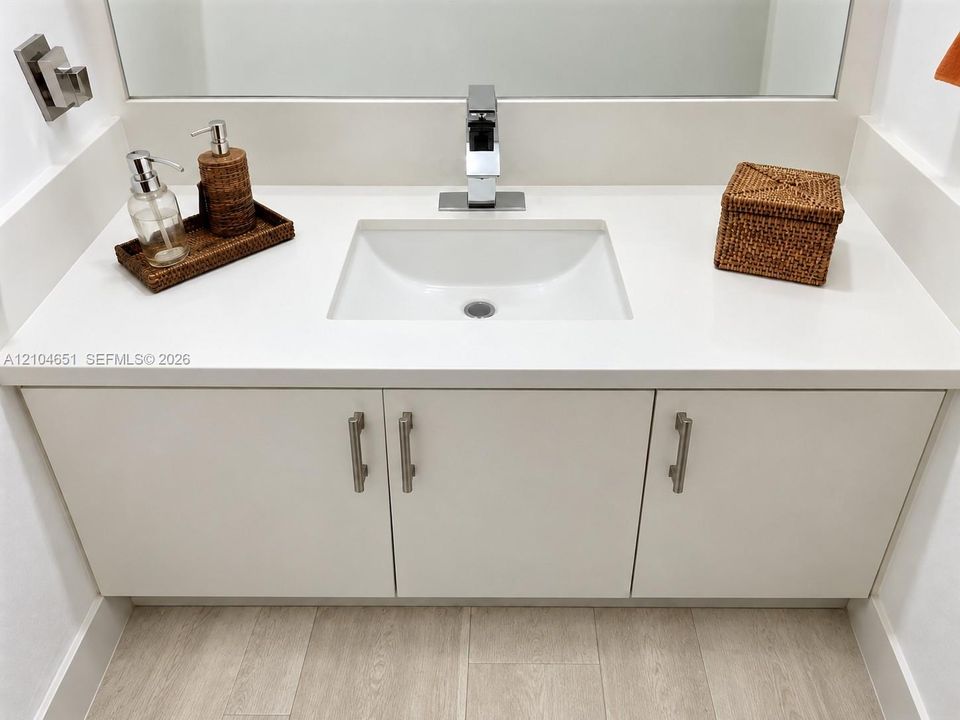 Floating vanity featuring a solid-surface countertop, integrated rectangular sink, chrome single-handle faucet, and matte silver hardware