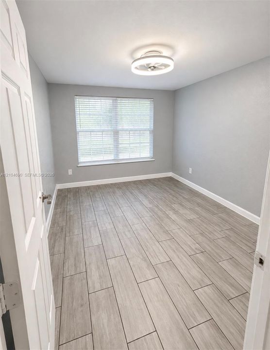 Room featuring neutral wall paint, wood-finish flooring, a contemporary circular flush-mount ceiling light, and a double-pane window with horizontal blinds