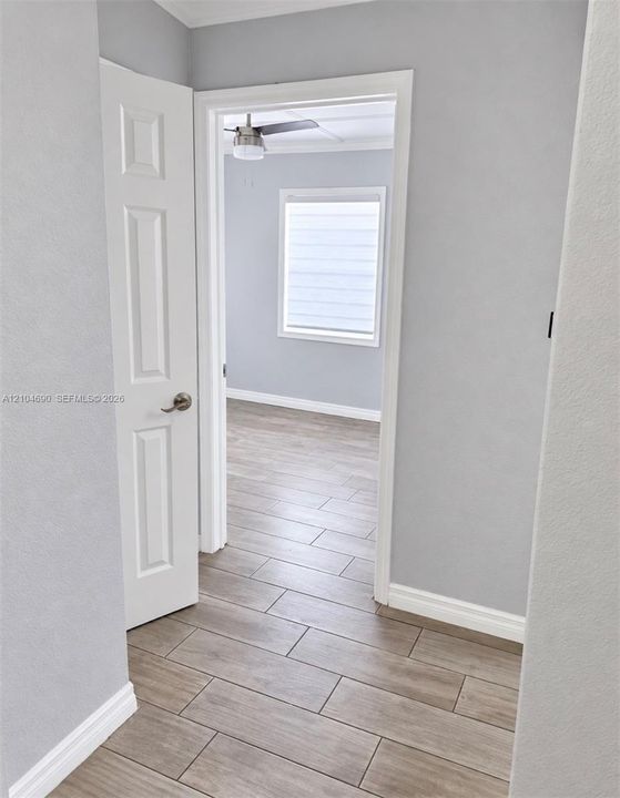 Interior space featuring neutral wall paint, wood-finish tile flooring, a six-panel door with metallic hardware, and a ceiling fan with integrated lighting