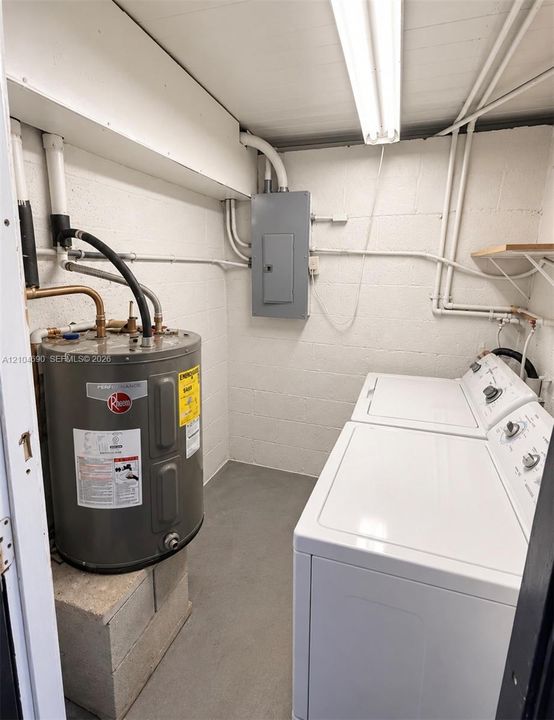 Utility space featuring a water heater, electrical service panel, laundry appliances, and painted concrete masonry block walls