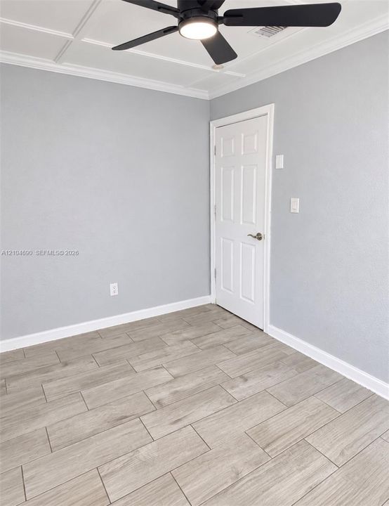Coffered ceiling featuring a matte black ceiling fan with integrated lighting, wood-finish tile flooring, and a six-panel door