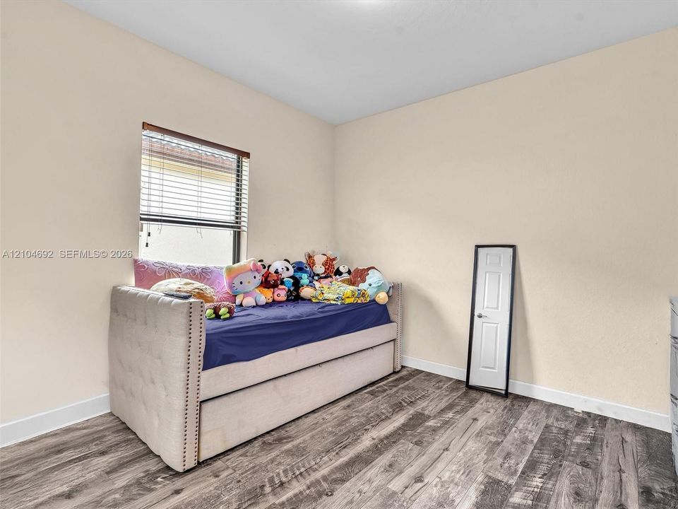 Room interior featuring wood-finish flooring, neutral wall paint, and a window with horizontal blinds