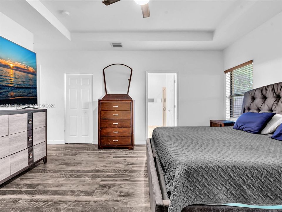 Tray ceiling with an integrated ceiling fan, wood-finish flooring, and window blinds