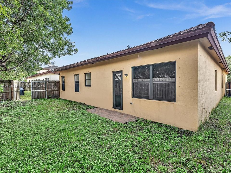 Stucco exterior featuring a tile roof, paved rear patio, single-light glass door, and wooden perimeter fencing