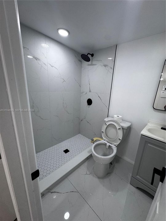 Walk-in shower with hexagonal tile floor, wall-mounted showerhead, and black fixtures