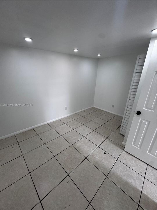 Recessed ceiling lighting, light gray wall finishes, square tile flooring, and a white paneled door