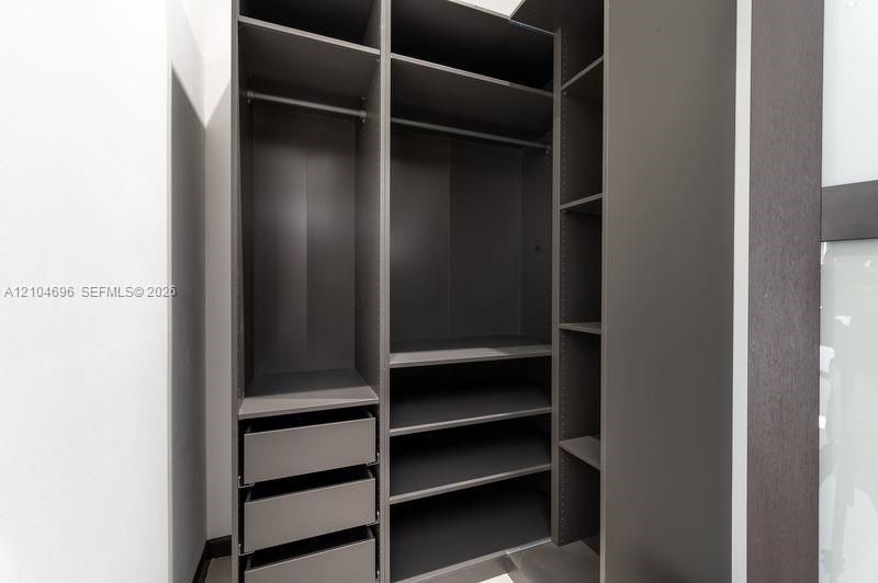 Custom storage system featuring dark wood-finish cabinetry, integrated shelving, tiered drawer units, and metal garment rods