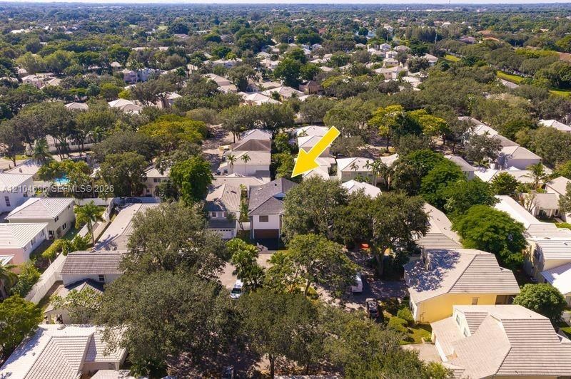 Aerial perspective featuring a two-story residence with a multi-hipped roof, paved driveway, attached garage, and mature tree canopy