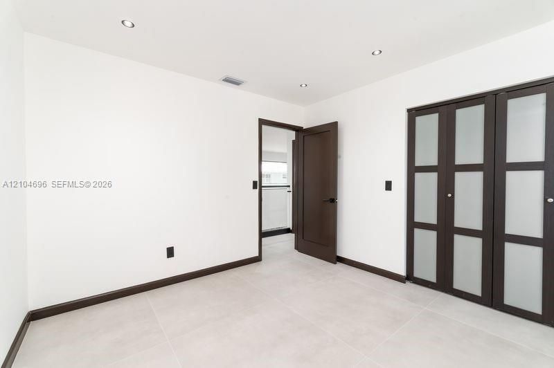 Interior space featuring light-toned tile flooring, recessed ceiling lighting, a dark-finish interior door, and a built-in closet with frosted glass panels