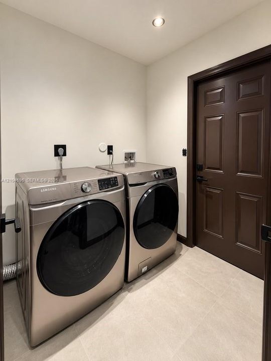 Laundry area featuring large-format tile flooring, recessed ceiling lighting, and a six-panel dark wood-finish door