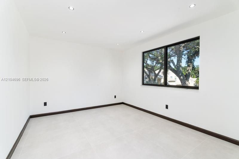 Interior room featuring large-format tile flooring, crisp white walls, recessed ceiling lighting, and a single-pane window with a black frame