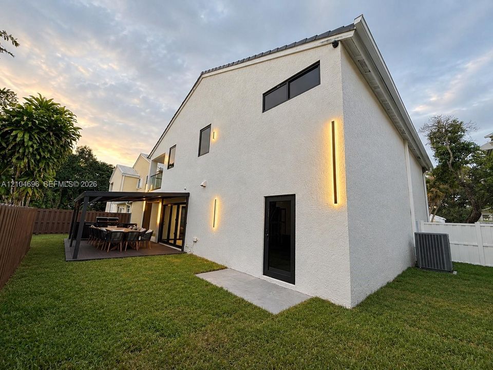 Stucco exterior featuring vertical linear wall sconces, a covered patio with dark-finish decking, and black-trimmed windows and doors