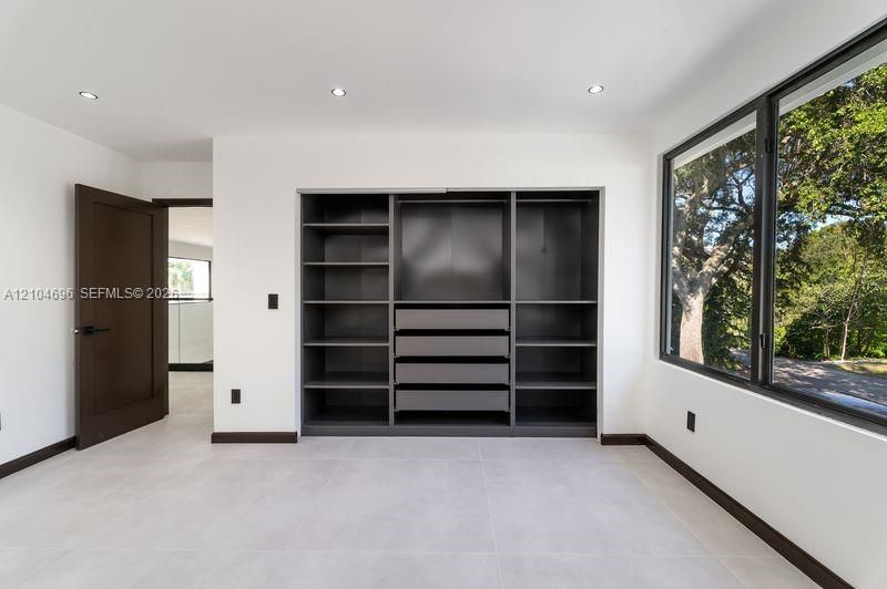 Built-in dark-toned cabinetry with integrated shelving and drawers, large-format tile flooring, recessed lighting, and expansive window with dark metal framing