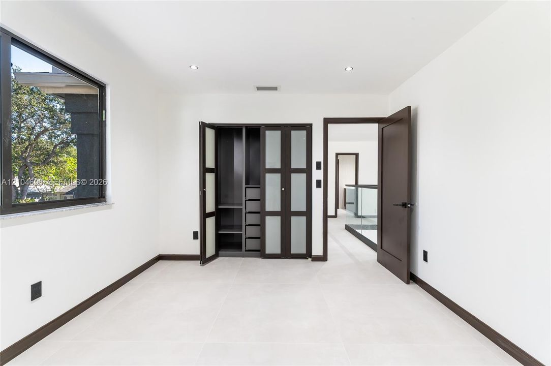 Room featuring large-format tile flooring, built-in wardrobe with frosted glass panel doors, dark-toned interior door, and multi-pane window
