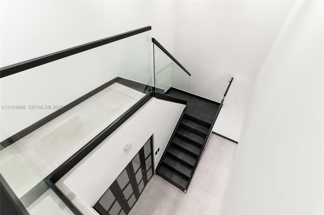 Staircase featuring dark-toned treads, glass railings with black metal trim, and a multi-panel door with frosted glass inserts