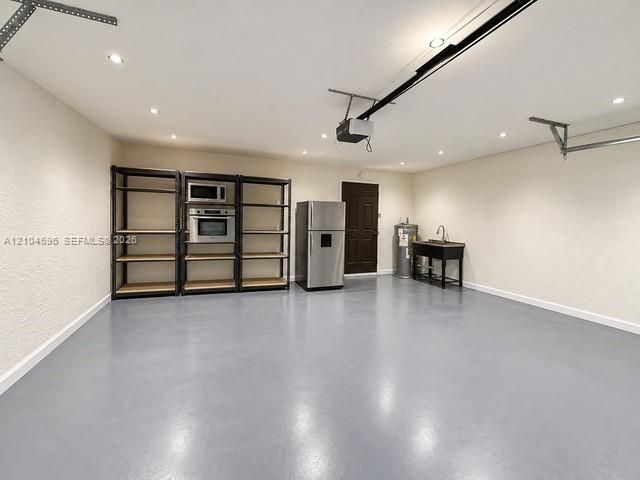 Garage space featuring an epoxy-coated floor, recessed lighting, a utility sink, and a stainless steel refrigerator