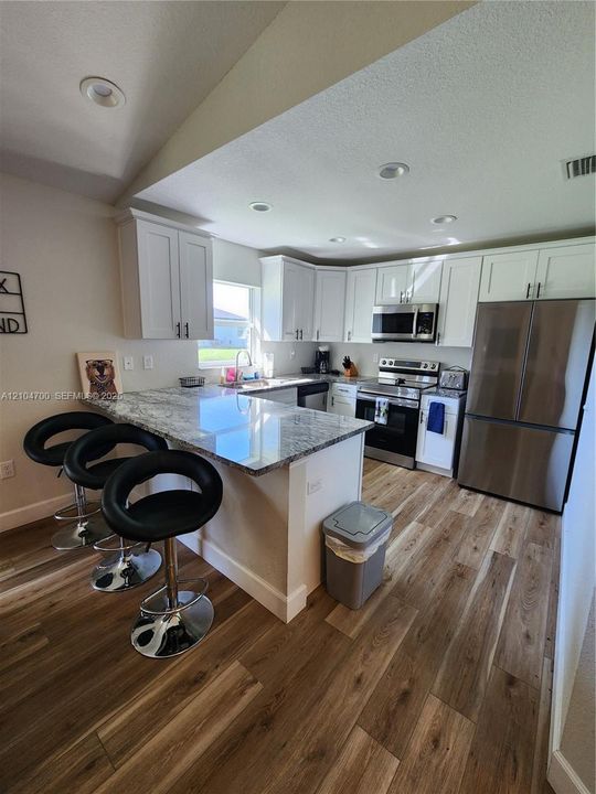 Kitchen featuring white shaker cabinetry, stainless steel appliances, granite-look countertops, a breakfast bar, and wood-finish flooring