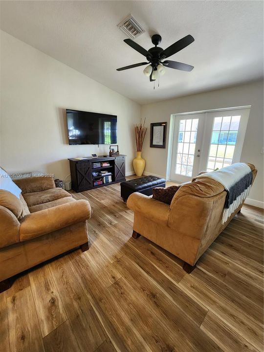 Vaulted ceiling with a black ceiling fan, wood-finish flooring, and double French doors with interior grids