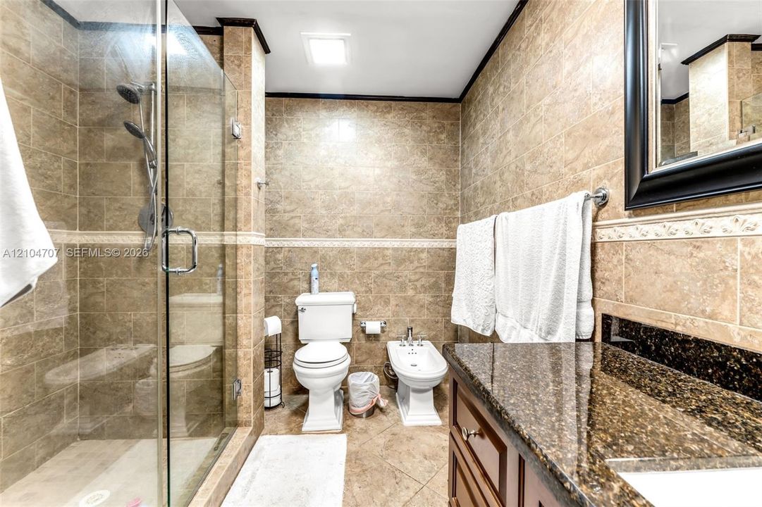 Bathroom featuring floor-to-ceiling stone-finish tile, glass-enclosed shower with a multi-function showerhead, dark stone-finish vanity countertop, and ceramic bidet