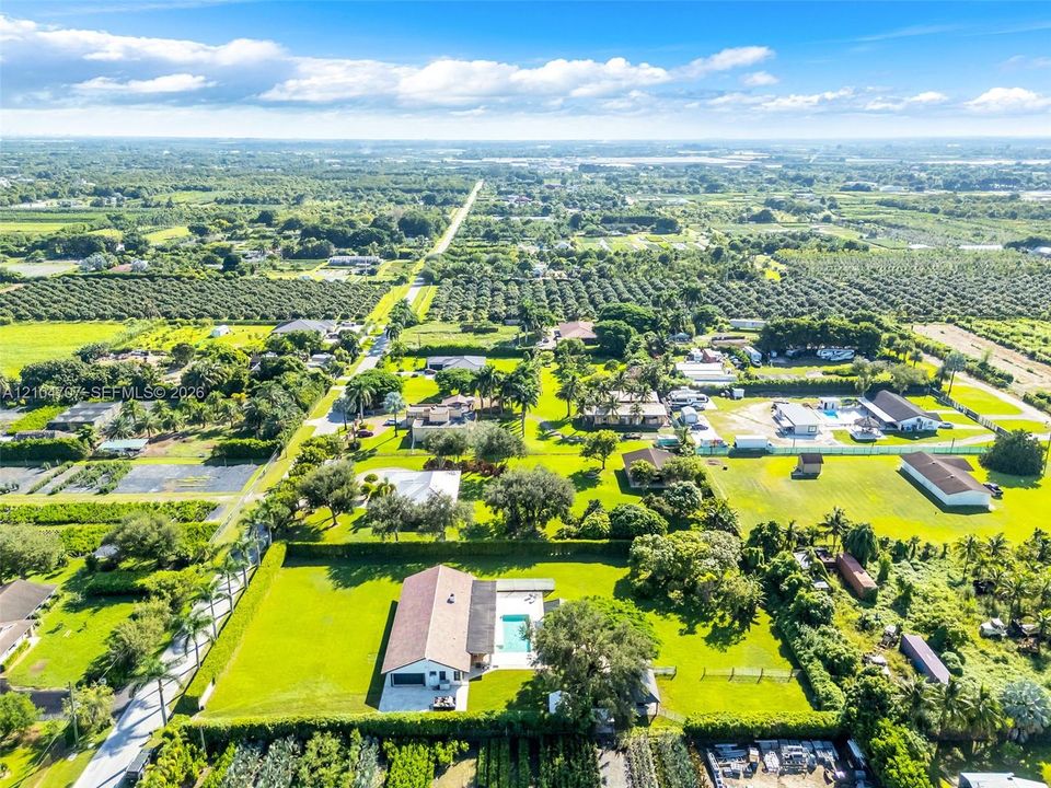 Aerial perspective featuring a sprawling parcel with expansive green space, a paved driveway, and an in-ground swimming pool