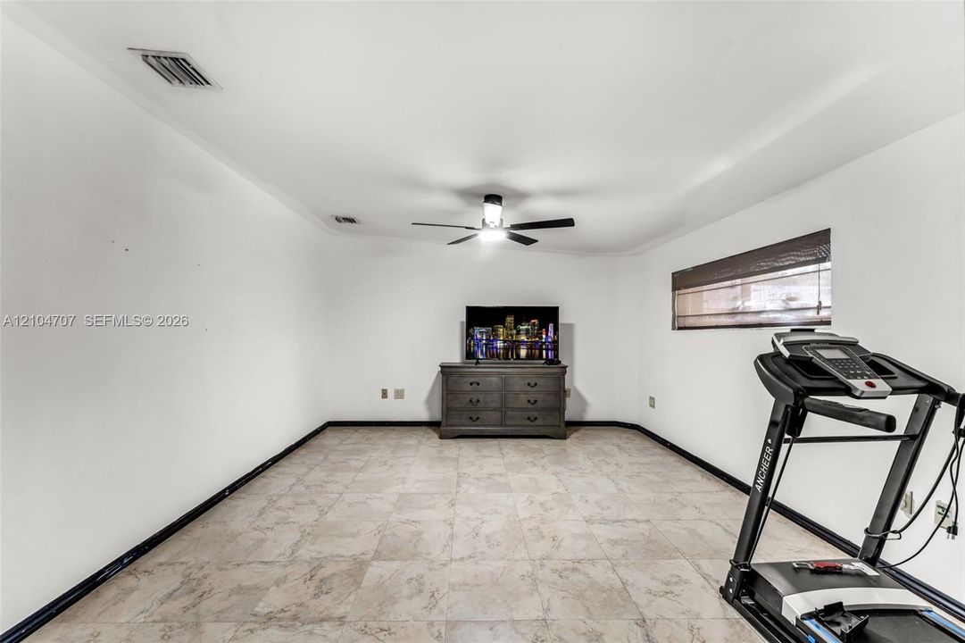 Room featuring large-format neutral tile flooring, a central ceiling fan with integrated light fixture, and horizontal window blinds