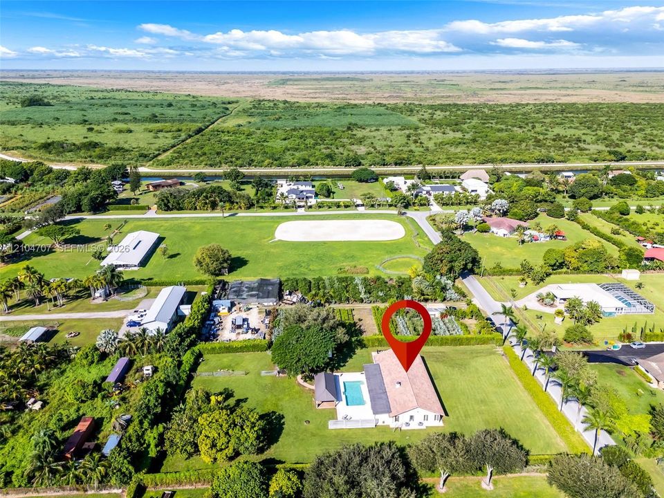 Aerial perspective of a sprawling property featuring a multi-pitched roof residence, a rectangular swimming pool, extensive manicured grounds, mature tree canopy, and established hedging