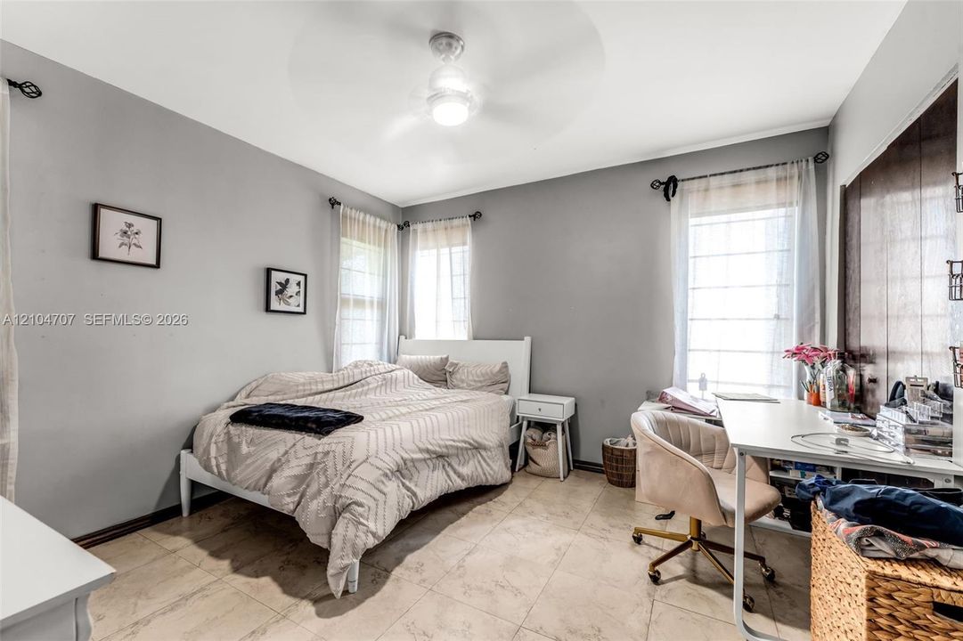 Neutral-toned room featuring large-format tile flooring, three windows with grid muntins, and a ceiling fan with integrated lighting