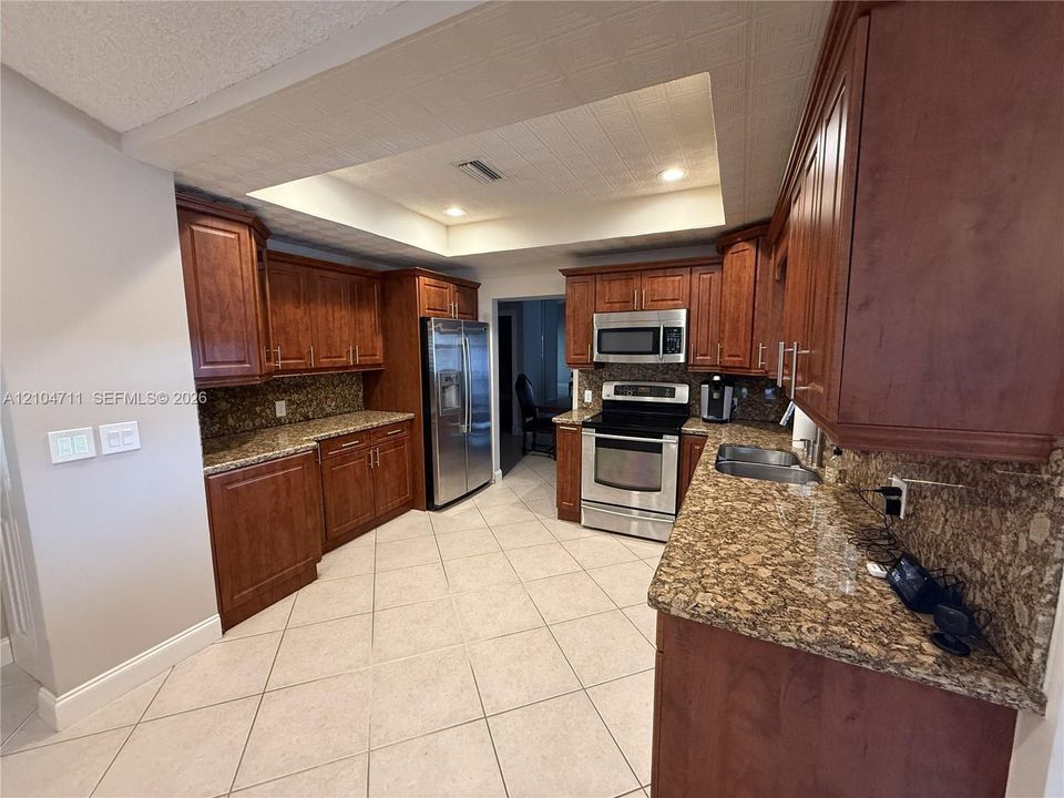 Kitchen featuring wood cabinetry, stainless steel appliances, granite countertops, and tiled flooring