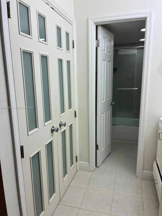 Double-panel doors featuring frosted glass inserts and chrome hardware, paired with a six-panel door opening to a tub and shower combination with tile flooring