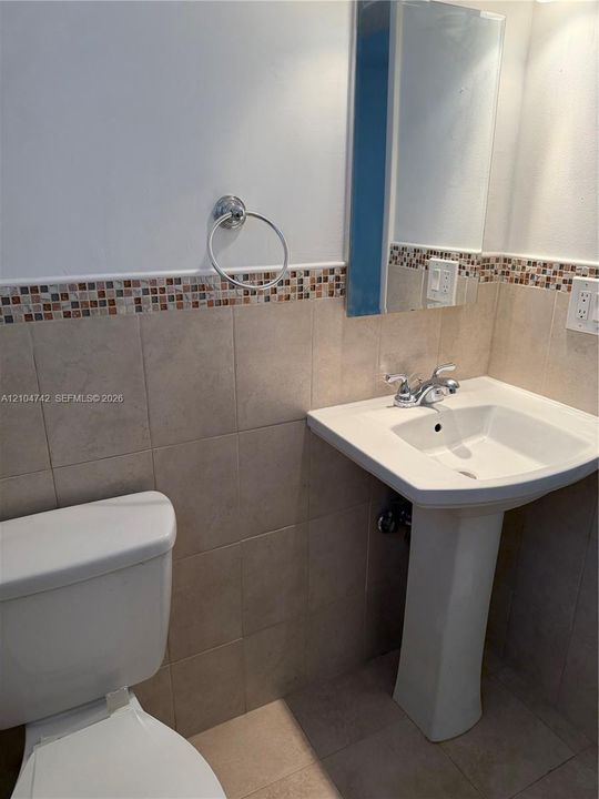 Pedestal sink with chrome faucet, mosaic tile accent, and wall-mounted mirror