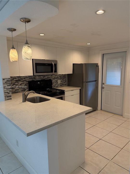 Kitchen featuring an island with an integrated sink, stainless steel appliances, white cabinetry, a tiled backsplash, and recessed lighting