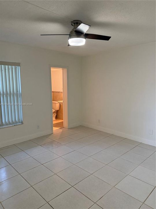 Neutral-toned tile flooring, white walls, and a ceiling fan with integrated lighting
