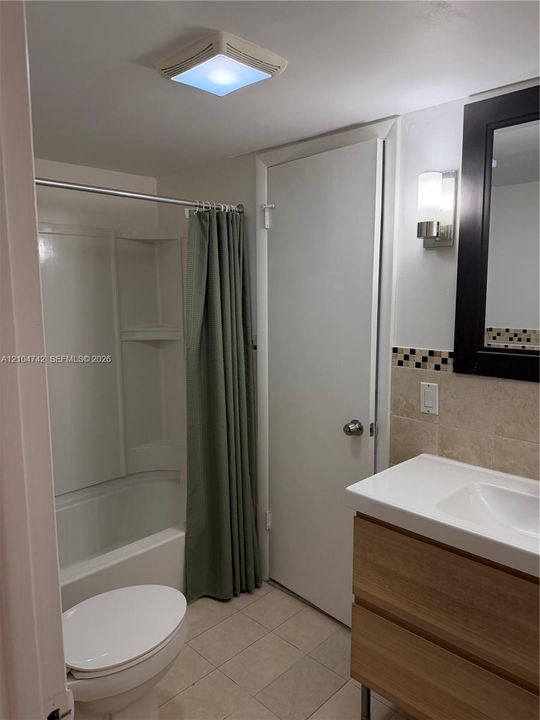 Modern bathroom featuring a wood-finish vanity with an integrated sink, tiled flooring, and a tub with shower combination