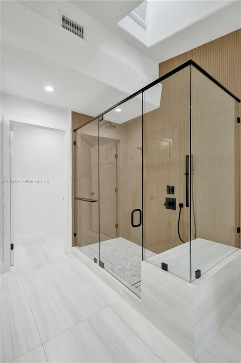 Glass-enclosed shower with matte black fixtures, integrated bench, skylight, and recessed lighting
