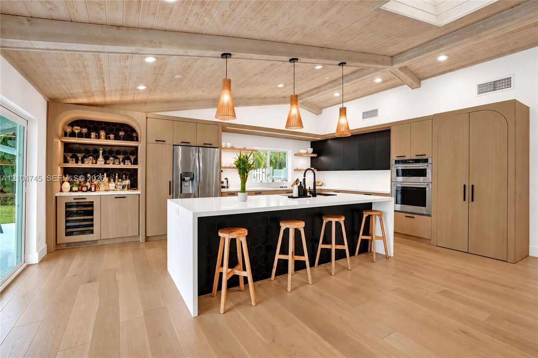 Expansive kitchen featuring a large island, wood-finish flooring, custom cabinetry, integrated appliances, and a built-in bar with beverage refrigeration